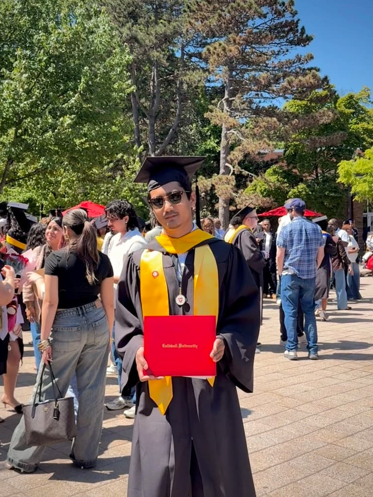 Pratiush at graduation in cap and gown, holding his Caldwell University diploma.